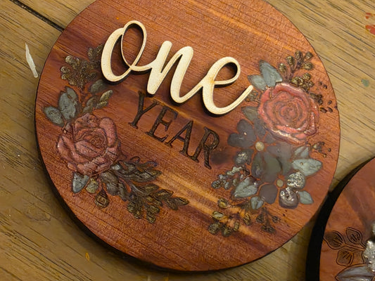 Wooden plaque with floral designs and 'One Year' text on a wooden surface