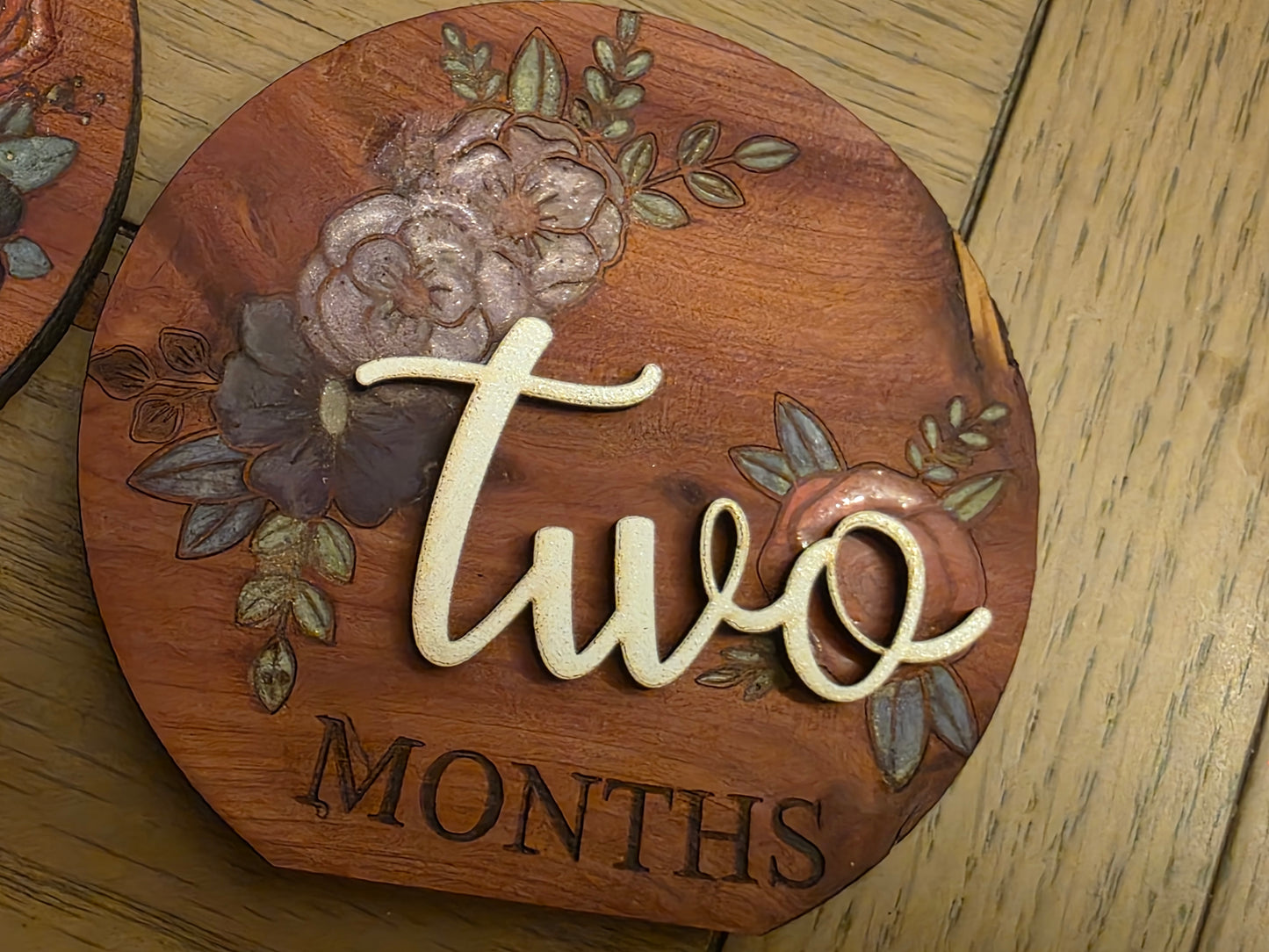 Wooden plaque with floral design and 'two months' text on a wooden surface